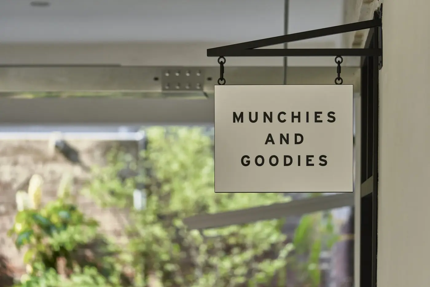 A shop sign hanging by a window with green leaves outside