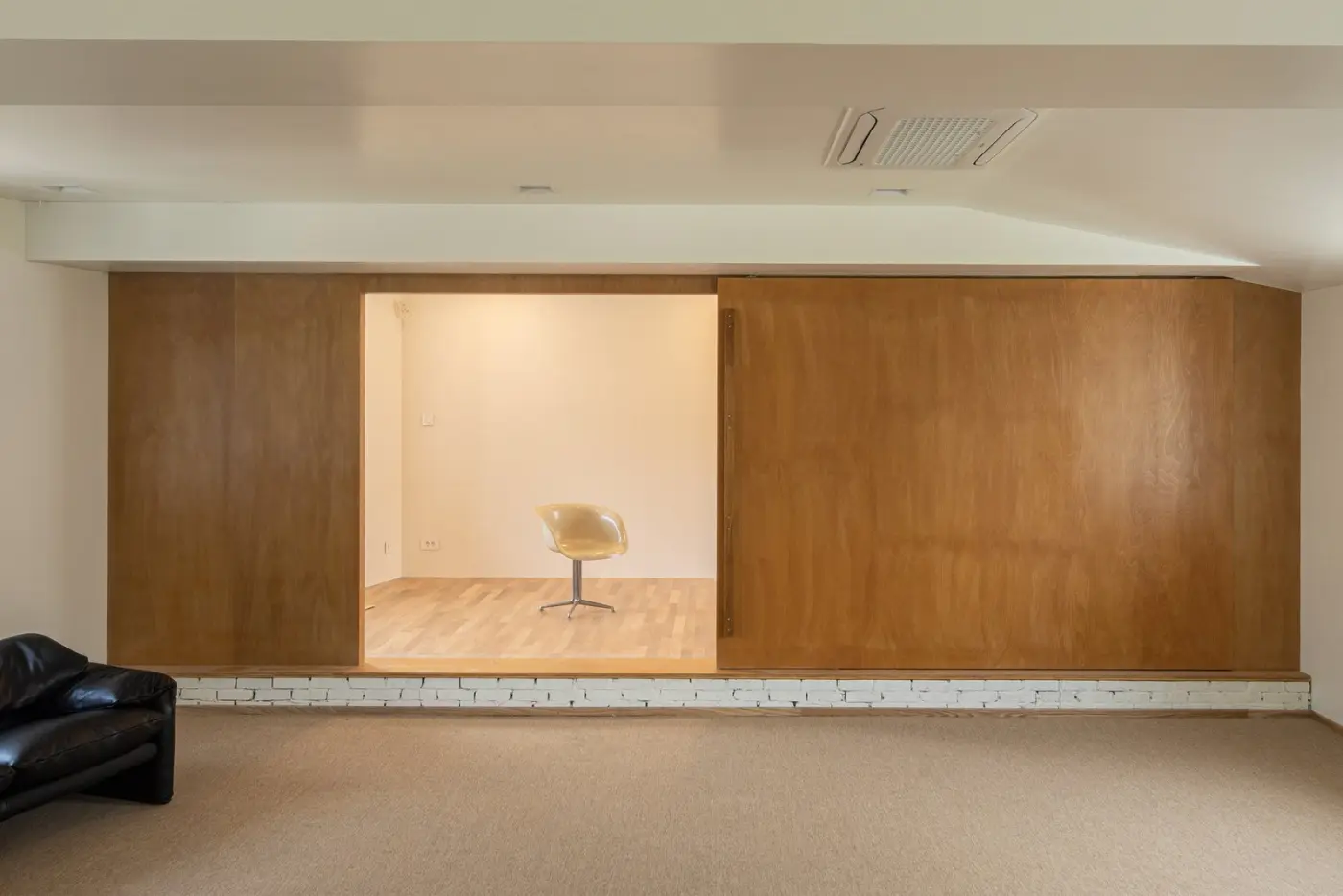 A bright empty room with a single chair between wood-panelled walls