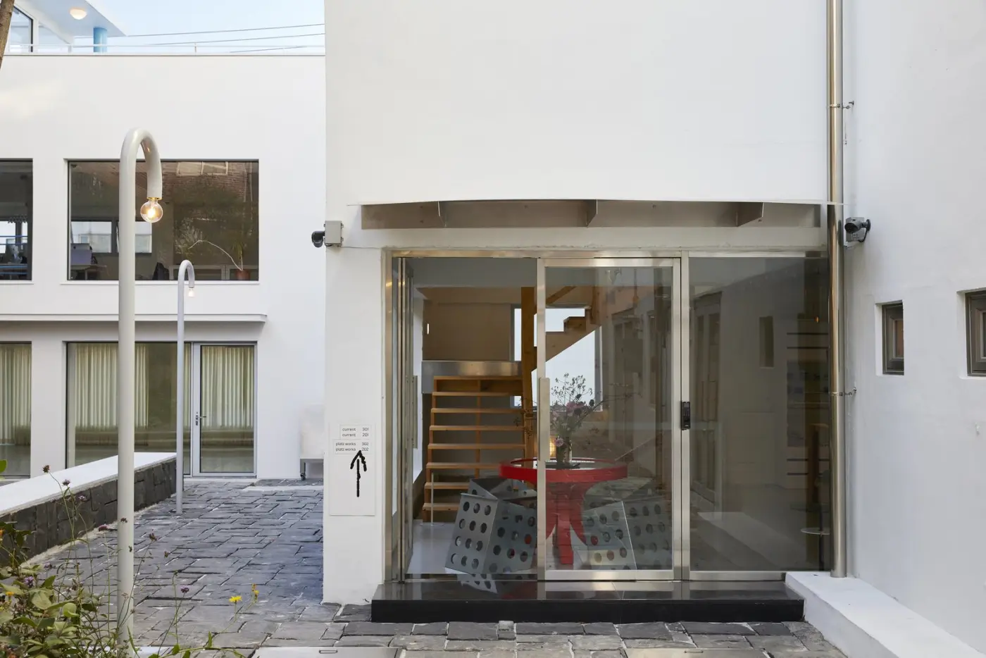 Entrance of a white building with a wooden staircase visible behind glass doors